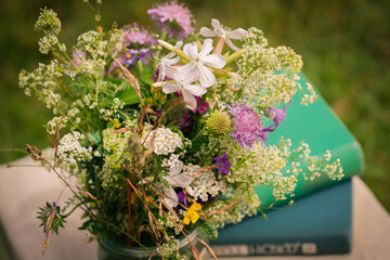 A beautiful bouquet of wildflowers and the books on a soft green background of summer garden.