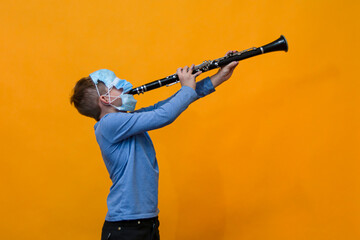 Boy playing the clarinet wearing masks, orange background. - obrazy, fototapety, plakaty