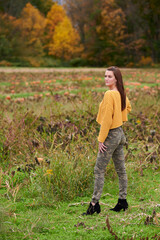 Adorable young woman in yellow crop sweater and camouflage pants stands in a pumpkin patch on farm - autumn holidays thanksgiving or Halloween themed