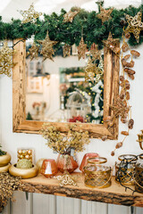 Mirror on the wall and a wooden stand decorated for Christmas with candles, vases, golden pine cones and сonifer branches 