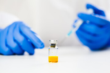Yellow ampoule vaccine liquid vial on table,hands in blue protective medical gloves holding syringe...