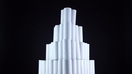 Obraz premium Empty toilet paper rolls on black background. Pyramid of hygiene items, empties toiletries exhausted during Covid-19 coronavirus epidemic lockdown. Empty stocks at quarantine and self-isolation.