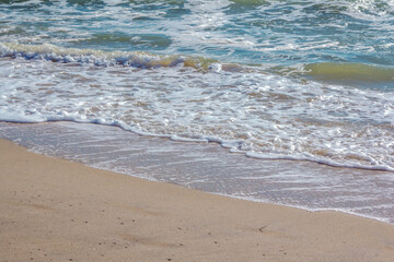 Landscape with stormy sea - clear water and foam - wave, covering sandy beach.