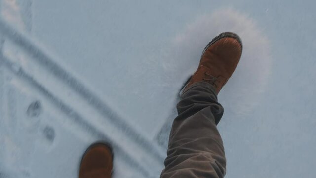 Feet of a man walking on loose snow with a view from above.A walk on a snowy winter evening.