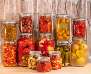 Canned vegetables, fruits and berries with spices, in beautiful glass jars. On a wooden table.