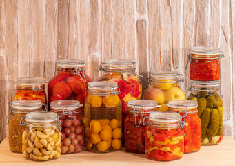 Canned vegetables, fruits and berries with spices, in beautiful glass jars. On a wooden table.