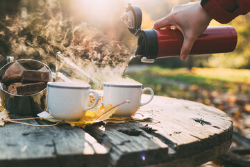 Early morning picnic in forest in late autumn. Cookies and hot tea woman pouring from thermos...