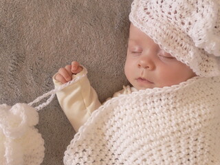 Sweet sleeping baby girl dressed in hand made crochet clothes and hat. Little princess with alabaster skin. Pale face baby closed eyes. 