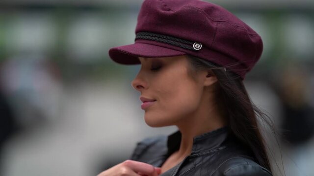 Close-up portrait of a beautiful female model in a purple cap and leather jacket posing in a public place. Located on one of the streets of the city.