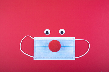 a red foam nose lies over a face mask, symbol for the restriction to carnival due to corona virus