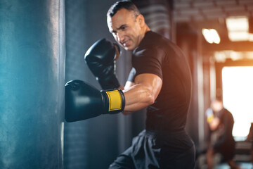 athletic sport man boxer training with punching bag or exercising in gym