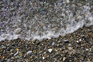 Multicolored pebbles with foaming sea waves