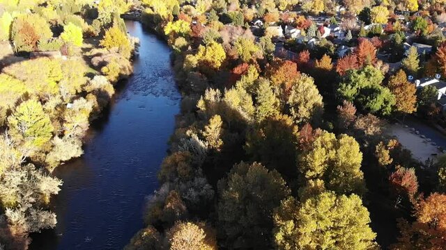 Flying over river and trees in fall color by residential neighborhood.