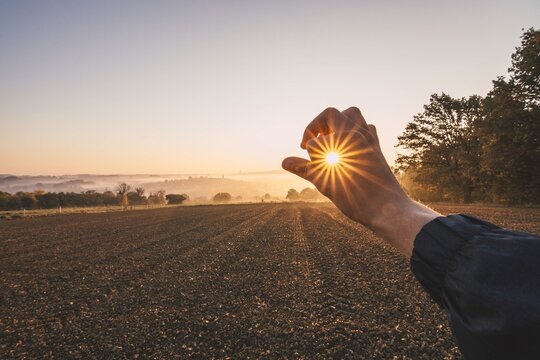 Optical Illusion Of Man Holding Sun On Field Against Sky During Sunset