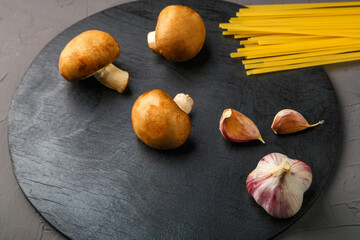 On a gray background on a black round stand, mushrooms and garlic pasta.