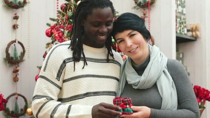 Multiracial family portrait. A pregnant woman and her African American husband hold small santa's shoes in their hands. Happy couple posing, smiling and laughing. - Powered by Adobe