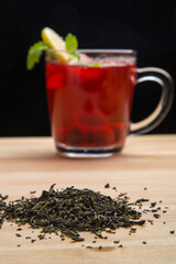 A cup of berry tea with lemon and tea leaves scattered on the table.