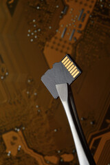 Close-up of a Micro SD memory card against the background of a microcircuit, clamped with tweezers.