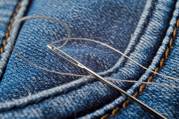 Close-up shot of needle with thread on jeans material. Close-up.