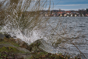 wave splashes at the shore of big ploner lake in background city of ploen,