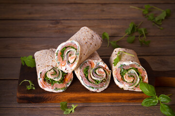 Salmon and cream cheese wraps. Rolls with smoked salmon, basil and rocket salad. Burrito on serving board