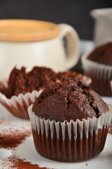 Chocolate muffin with a crack on top, sprinkled with cocoa on a white marble board, on the dark background.