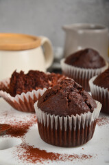 Chocolate muffin with a crack on top, sprinkled with cocoa on a white marble board, on the grey background.