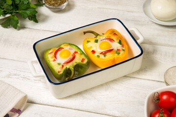 Bell peppers stuffed with vegetables, baked with cheese and quail eggs in a casserole on a white rustic table.