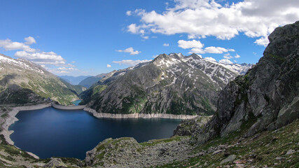 Fototapeta na wymiar A panoramic view on an artificial, dam lake stretching over a vast territory around Alps in Austria. Lake is shining with navy blue color. In the back there are a few glaciers. Controlling the nature