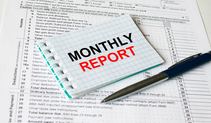 Obraz premium Notepad with text Monthly Report lying on financial tables with a pen