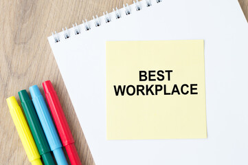 the inscription on the yellow sheet for notes text BEST WORKPLACE which is attached to the notebook on the table.