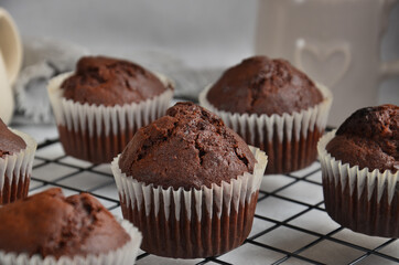 Chocolate muffins on a black metal grill on a gray background.