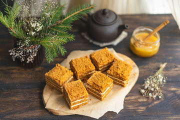 Layer Honey sliced Cake with pastry cream filling on wooden cutting board, dark wooden table near window. Close up view, copy space. Organic homemade dessert.