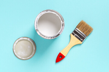 New natural bristle brush with wooden handle, open white paint can and lid on a cyan blue...