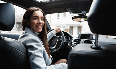 Elegant woman driver looking at backseat, smiling happy, asking passanger fasten seatbelt. Businesswoman talking to person in her car, driving at work