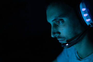 Un chico joven en una habitación oscura jugando al ordenador o trabajando como hacker con su portátil.