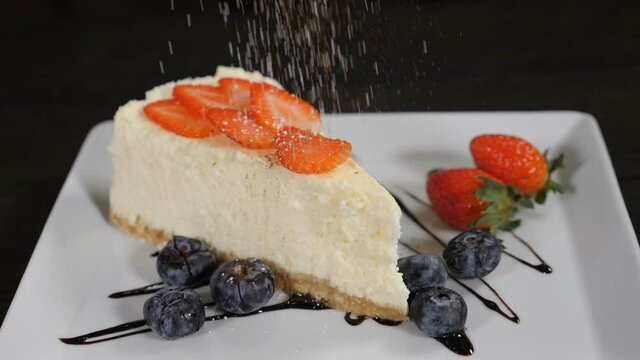 Chef serving delicious cheesecake sprinking cinnamon. Slow motion. Appetizing cheese cake with straberries and blueberries placed on white plate. Cacao powder falling. Dessert in restaurant. Full hd
