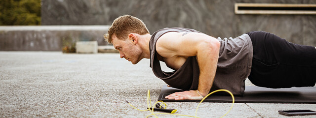 Photo of an athletic guy doing push ups. Athlete doing fitness training outdoors. Workout during lockdown outside the gym.