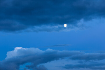 Background of mystery cumulus clouds with moon on a blue sky at evening blue hour after sunset. Telephoto zoom photo shot