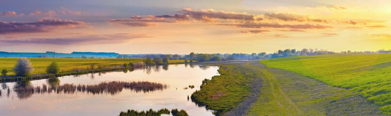 Naklejka na ściany i meble Wide panorama with river, field and picturesque sky at sunset