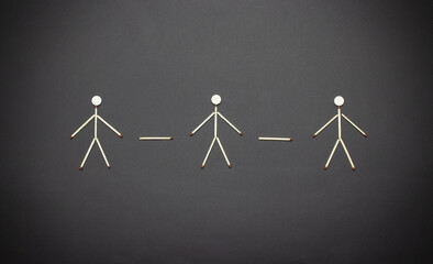 The concept of social distancing in the form of three matchstick men on a black background.Keep your distance in a public place to protect yourself from the COVID-19 coronavirus epidemic.