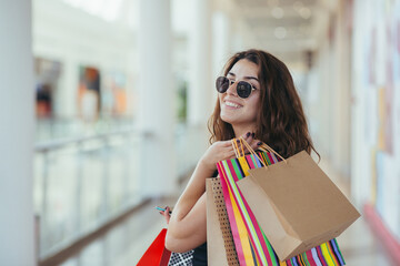 Cheerful lady in stylish black dress carrying on colorful shopping bags while walking at store....