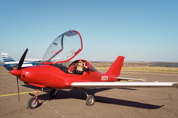 Young fashionable woman pilot in headset ready to fly in small red airplane. Beautiful life,...