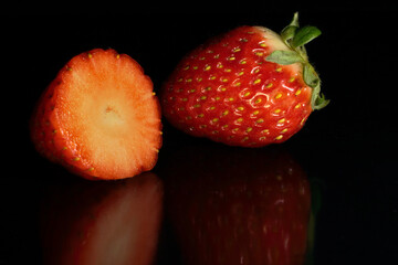 Two whole and split strawberries on black background