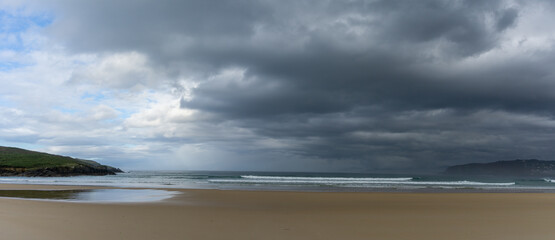 panorama of an empty and large beautiful golden sand beach underneath a bad weather sky
