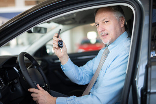 Man showing the key of his new car in a car dealer saloon