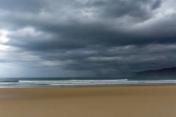 empty and large beautiful golden sand beach underneath a bad weather sky