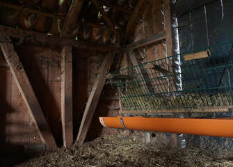 Inner part of a rustic old wooden sheepfold. Hay on the ground and in the feed trough. Orange water...
