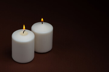 Fototapeta na wymiar Two white candles flame burning on dark background with copy space for text.