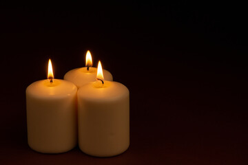 Fototapeta na wymiar Three white candles flame burning on dark background with copy space for text.